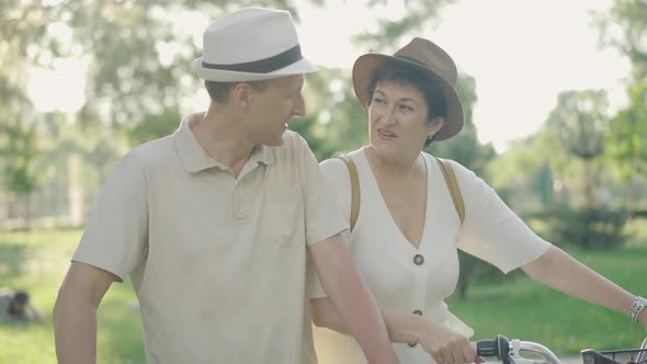 Charming Mid-adult Caucasian Couple Sitting on Bicycles in Sunlight and Talking. Laughing Man and