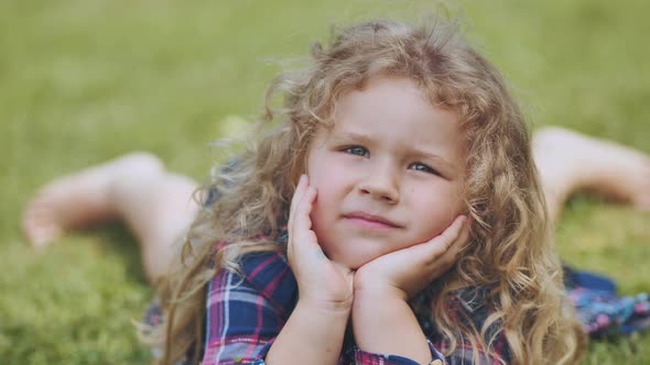 A Little Curlyhaired Girl Lies on the Grass in the Garden