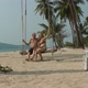 a Man and a Woman in a Swimsuit Swing on a Swing Suspended From a Palm Tree on the Beach of the Sea - VideoHive Item for Sale