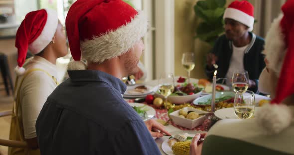 Happy caucasian man in santa hat celebrating meal with friends at christmas time