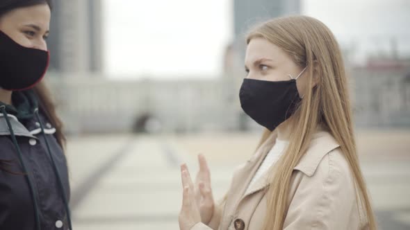 Close-up of Young Woman in Covid Face Mask Stopping Friend From Hugging. Portrait of Serious