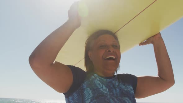 Happy senior african american woman walking with surfboard on sunny beach