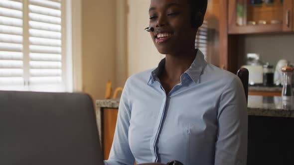 African american woman wearing phone headset having a videocall on laptop while working from home