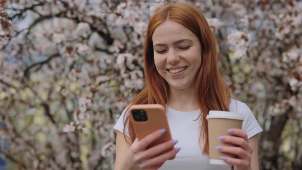 Smiling Lady with Cup of Coffee Using Phone in Spring Park