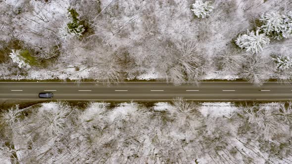 Flying over a driving car by drone, tracking it when it drives through a winter forest landscape