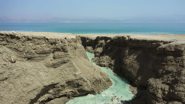 Dead Sea Hot Springs dramatic aerial fly in above desert canyon landscape over crystal clear warm wa