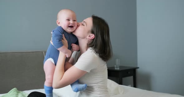 Caring for Infant, Mother Raising Son in Arms Hugging and Kissing