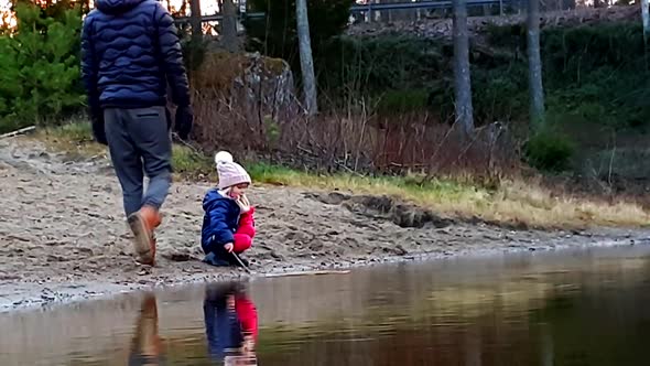 young girl on the beach playing with stick in the water, father joining in, cute moment with autumn