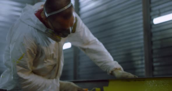 Man in Overalls and Protective Mask Paints Metal Structures with a Roller Yellow