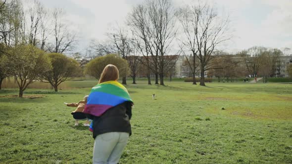 Stylish LGBT Couple Playing with Their French Bulldog in Park Wearing Rainbow Flag