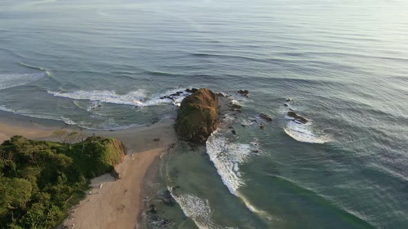 Cinematic aerial orbit around a giant rock on the tip of narrow peninsula. Playa Ventanas and playa