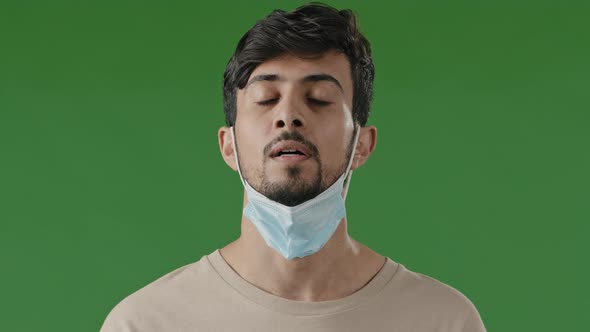 Tired Young Hispanic Man in Medical Mask on Green Background in Studio Arab Guy Take Off Respirator