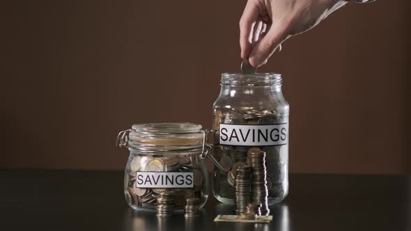 Hand of Man Putting Coin Into Glass with Savings