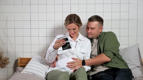 Young Family Looks at Ultrasound Picture and Strokes Belly