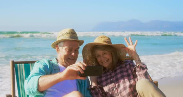 Front view of active senior Caucasian couple taking selfie with mobile phone on the beach 4k