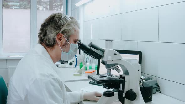 Laboratory Assistant Looks Into a Microscope and Twists It in a White Laboratory