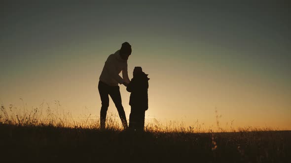 Silhouette Happy Mother and Little Son Are Playing Around While Walking Outside at Sunset