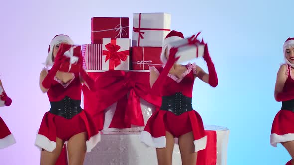 Group of Young Sexy Snow Maidens in Short Red Suits and Hats Are Dancing with Gifts in Their Hands