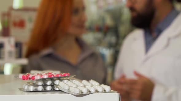 Pharmacist Taking Blister of Pills From the Counter, Talking To His Female Customer
