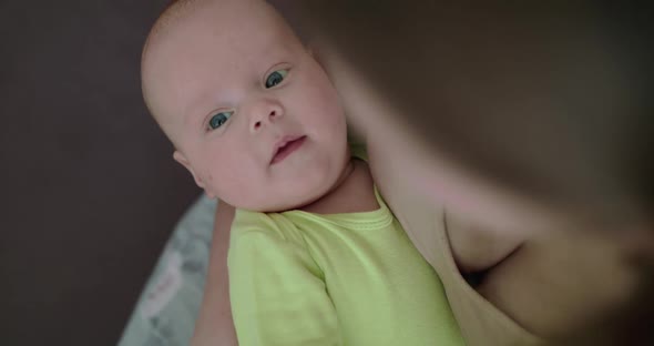 Top View of Sated Newborn Baby Rejoices at Mother's Hands and Looks at Camera