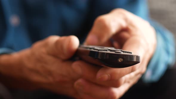 Close-up of a senior's hand holding a TV remote control switching buttons.