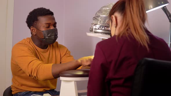 African American Man in Protective Mask in a Beauty Salon Takes Care of Nails From a Manicure Master