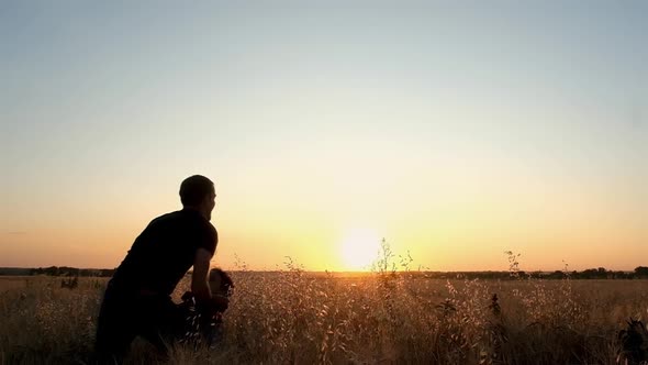 young father catches his son running in a field at sunset.