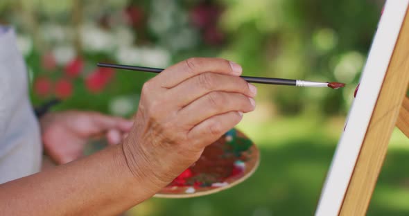 Video of hands of biracial senior woman painting in garden
