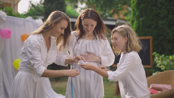 Joyful Young Woman and Teenage Girl Measuring Waist of Pregnant Mother in Slow Motion Laughing