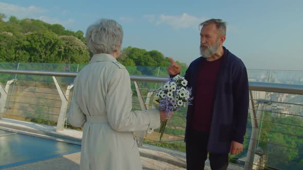 Elderly Bearded Man and Woman with Flowers Quarreling Outdoors