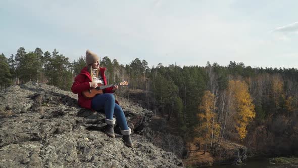 Caucasian Woman Sits on Rock and Plays the Ukulele