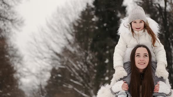 Mother Carrying Daughter on Shoulders Below Trees in Winter Wood