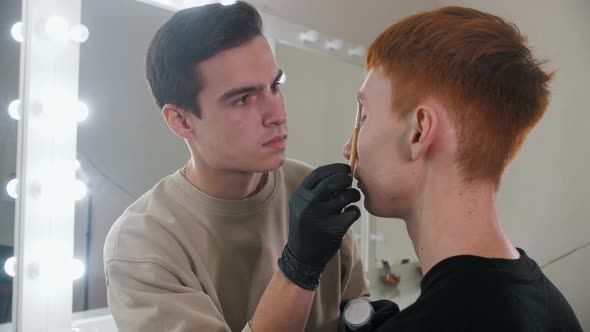 Brow Master Drawing Guiding Lines on the Eyebrows of His Male Client