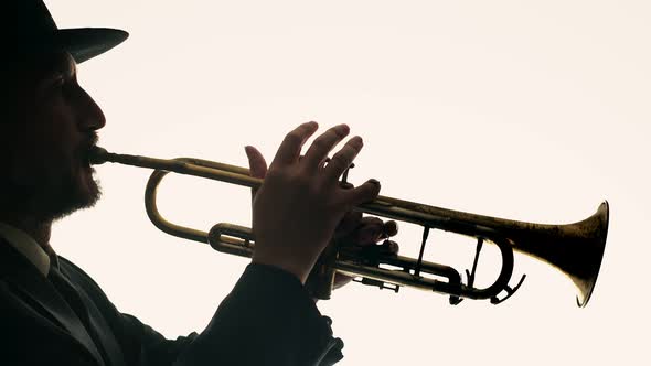 Male Musician in Hat and Suit Plays Trumpet and Dances on White Background Side View