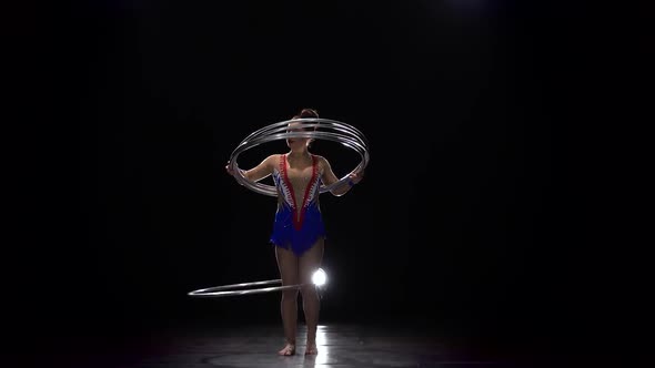 Gymnast in a Bright Outfit Twists a Hoop on Her Arm and Then on Her Leg