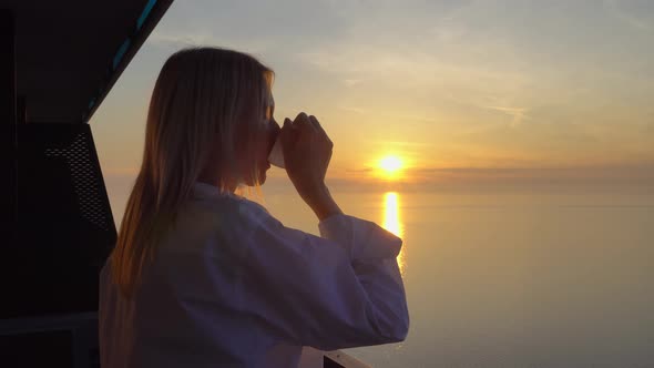 a woman admires the sunset over the sea, and drinks coffee on a high floor.