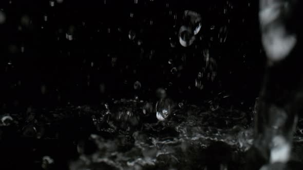 Pouring water on black surface against black background. Slow Motion. alt