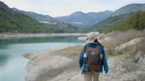 Young Woman in Trekking Gear Walks Away From Camera By Lake in Spain