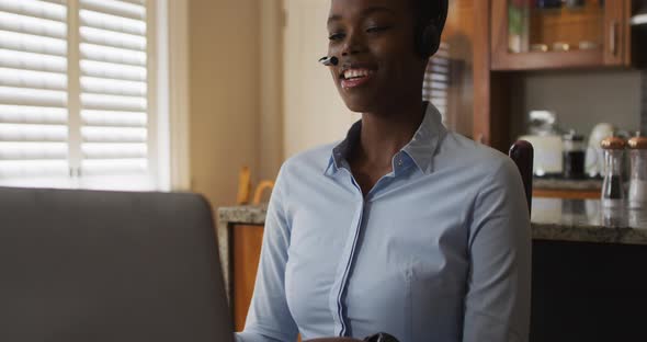African american woman wearing phone headset having a videocall on laptop while working from home