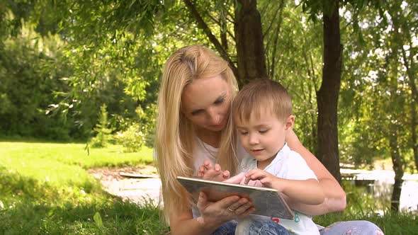 Happy Mother and Her Little Son Enjoying Playing on Tablet Computer in the Park
