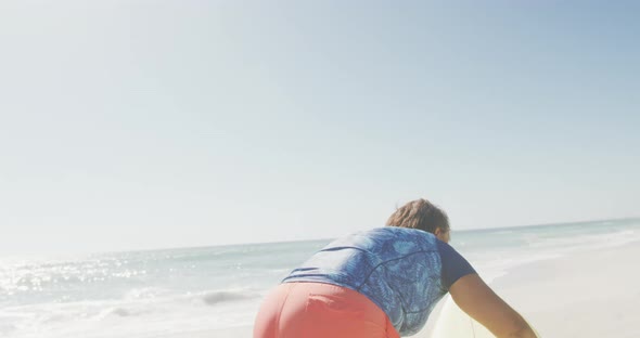 Happy senior african american woman carrying surfboard on sunny beach