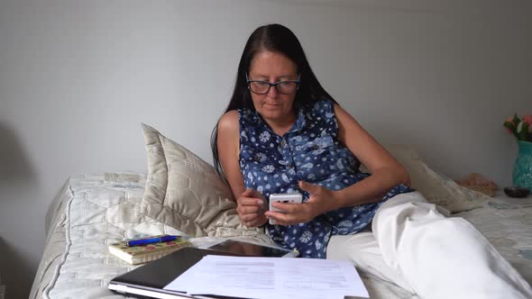 Businesswoman on work phone reading emails in bed, morning routine covid-19