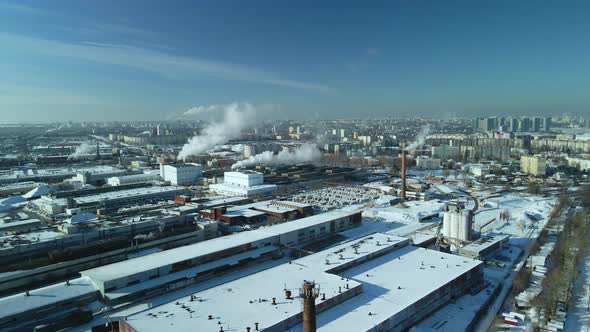 Factory buildings covered with snow. Factory smoke chimneys. There is a railway nearby.