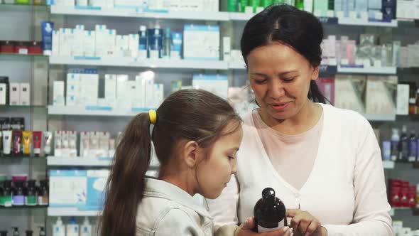 A Smiling Woman Chooses with Her Daughter Something in the Pharmacy