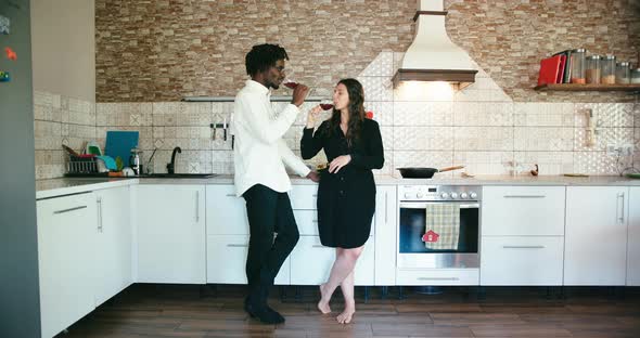 Young Couple Talk and Drink with Glasses of Wine Stand in Kitchen