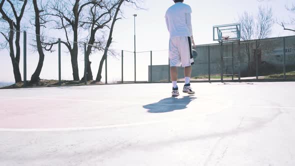 Portrait of a Basketball Player Walking on an Outdoor Basketball Court and Dribbling the Ball Slow