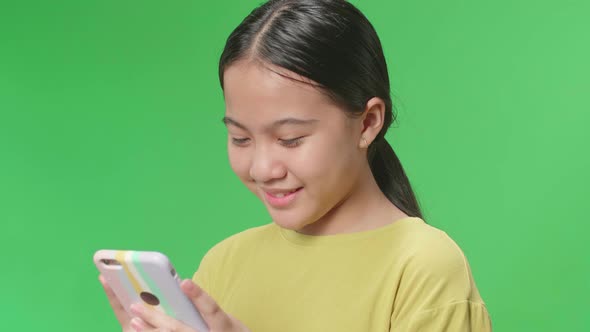 Smiling Young Asian Kid Girl Using Mobile Phone In Green Screen Studio