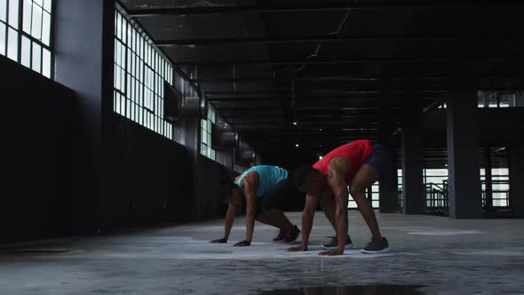 African american man and woman doing push ups jumping exercises in an empty urban building