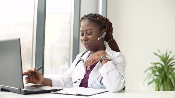 Young African American Woman Doctor with Headset Having Chat or Consultation on Laptop