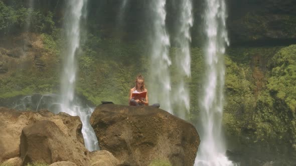 Lady Reads Diary on Rock Among Waterfall Streams